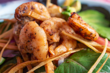 A closeup view of a pile of grilled shrimp on top of a salad, in a restaurant or kitchen setting.