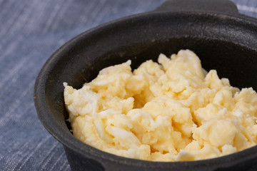 Scrambled egg in a traditional cast iron pot on a blue tea towel.  On a patterned tile surface