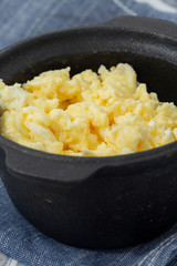 Scrambled egg in a traditional cast iron pot on a blue tea towel.  On a patterned tile surface