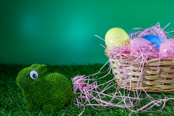 Easter eggs on a basket with grass and a green rabbit made of grass with green background for happy easter celebration