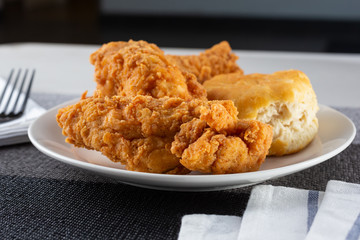A view of a plate with fried chicken and biscuit, in a restaurant or kitchen setting.