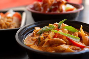 A closeup view of several Asian entrees, in a restaurant or kitchen setting, featuring a red curry bowl.