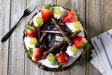 A top down view of a decorated chocolate and fresh fruit cake, in a restaurant or kitchen setting.