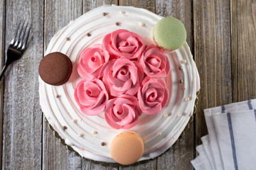 A top down view of a decorated cake with pink flower frosting designs and macaron cookies as toppings, in restaurant or kitchen setting.