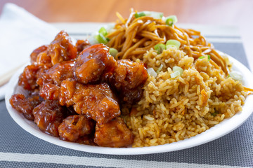 A view of a combo plate of a Chinese fast food restaurant, featuring orange chicken, chow mein and fried rice.