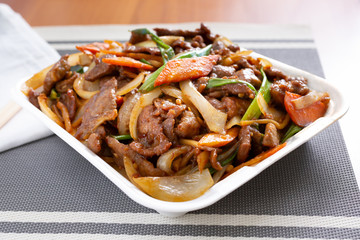 A view of a take out container plate of Mongolian style beef on display in a restaurant or kitchen setting.