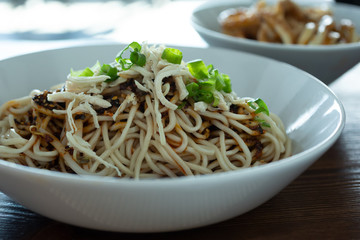 A view of a bowl of dan dan noodles with shredded chicken, in a restaurant or kitchen setting.