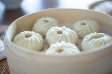 A closeup view of a bamboo steamer full of Chinese bao, in a restaurant or kitchen setting.