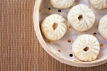 A top down view of a bamboo steamer of Chinese baozi, in a restaurant or kitchen setting.