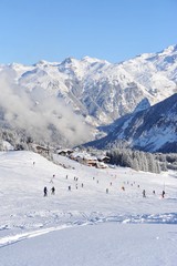 Fototapeta na wymiar Ski resort Courchevel in European Alps, with skiing people and chalets under the clouds in winter. Courchevel is one of the best resort and most famous one with it’s wide range of ski slopes. 