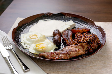 A view of a Salvadorean breakfast entree featuring eggs, steak, sausage, plantains, cheese and rice and beans.