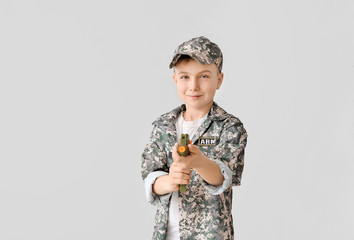 Cute little soldier with toy gun on light background