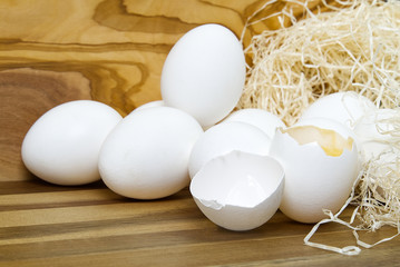 White chicken eggs and broken eggs on wooden board or table.