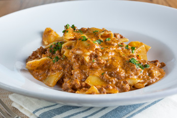 A closeup view of a plate of pappardelle bolognese, in a restaurant or kitchen setting.