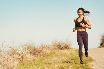 Full length of young muscular build woman jogging by the road.