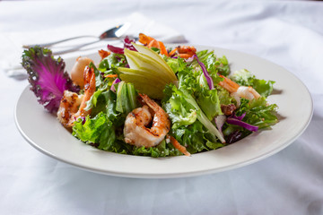 A view of a Mediterranean salad with shrimp, in a restaurant or kitchen setting.