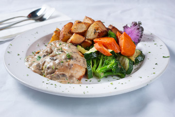 A view of a plate of chicken Florentine, with steamed veggies and roasted potatoes, in a restaurant or kitchen setting.