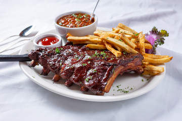 A view of a plate of baby back pork ribs, in a restaurant or kitchen setting.