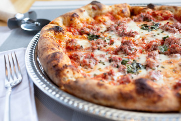 A closeup view of a rustic pizza pie in a restaurant or kitchen setting, featuring toppings such as sausage and herbs.