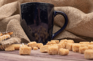 Dark blue ceramic tea mug, cookie sticks with chocolate and white icing and brown cane sugar pieces on a wooden background. Close up.