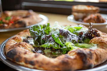 A view of several dishes on display in a restaurant setting, featuring a rustic pizza with mushrooms and gem lettuce greens as toppings.