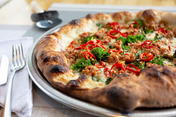 A view of a rustic pizza pie in a restaurant or kitchen setting, featuring toppings such as Spanish chorizo sausage, broccoli and red peppers.