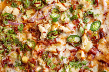 A top down view of a barbecue chicken and jalapeño pizza, in a restaurant or kitchen setting.