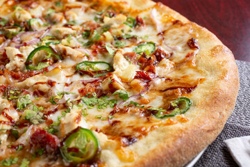 A closeup view of a barbecue chicken and jalapeño pizza, in a restaurant or kitchen setting.