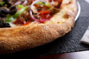 A closeup view of a supreme pizza pie crust, in a restaurant or kitchen setting.