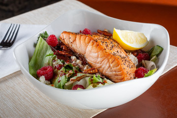A view of a bowl of salmon fillet salad with raspberry vinaigrette, in a restaurant or kitchen setting.