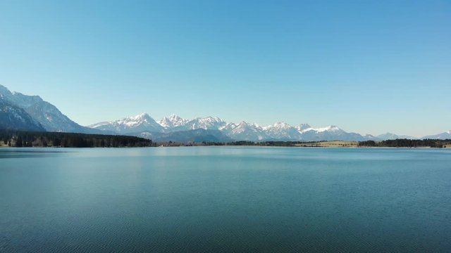 Hoch &uuml;ber dem Bannwaldsee mit Schwenk &uuml;ber die Tannheimer Berge mit schneebedeckten Gipfeln im Fr&uuml;hjahr