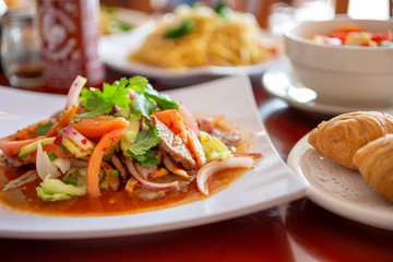 A view of several prepared dishes in a restaurant setting, featuring a Thai beef salad dish.