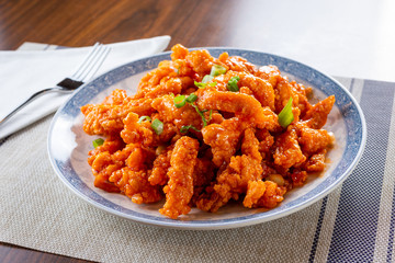 A view of a plate of orange chicken in a restaurant or kitchen setting.