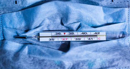 the medical thermometer shows the highest temperature on the blue background of the protective mask.