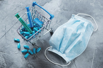 Decorative shopping cart with pills, syringes and medical mask on a grey concrete background, selective focus, studio shot