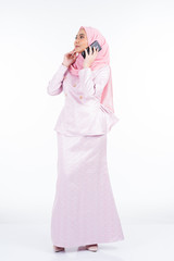 An attractive Muslim lady wearing traditional outfit and hijab, using her smartphone for selfie, chat and making call isolated on white background