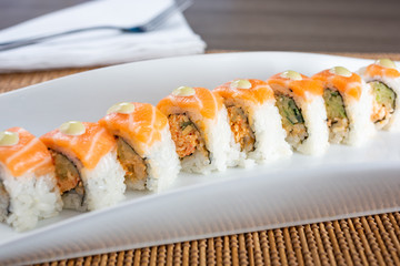 A side view of an orange dragon roll sushi plate, in a restaurant or kitchen setting.