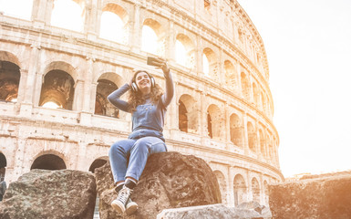 Fototapeta na wymiar Young woman taking selfie in front of Coliseum in Rome while listening music with hedphones - Happy girl having fun with technology trends - Travel, real people and tech concept - Soft focus on face