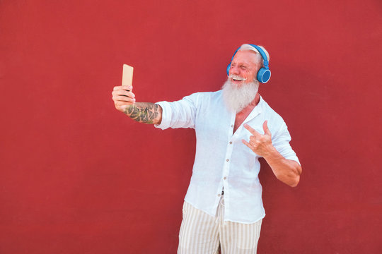 Senior hipster man using smartphone app for creating playlist - Trendy tattoo mature guy having fun with mobile phone technology - Joyful elderly lifestyle concept - Focus on left hand