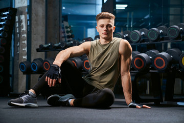 Muscular man posing on floor in gym.