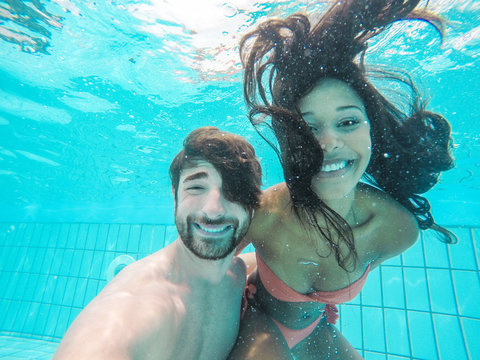 Travel couple taking selfie photo under the water in swimming pool - Young people having fun during summer vacation - Technology trends and influencers concept - Soft focus on man face