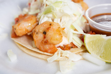 A closeup view of a shrimp taco, in a restaurant or kitchen setting.