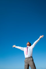 Businessman standing outdoors holding arms up facing the sun against clear blue sky