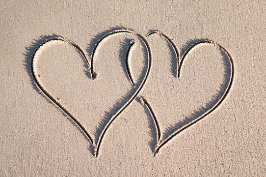 Pair of handwritten hearts drawn interlocking in smooth sand on a sunny beach