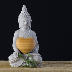 buddha figur hält ein hölzernes herz in seinen händen vor schwarzem hintergrund liebe ruhe mediation