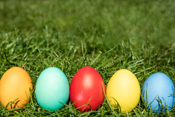 Fototapeta na wymiar Multi-colored Easter eggs on the grass, the background is blurred, shallow depth of field, selective focus. Easter holiday concept