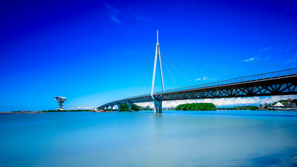 A modern bridge connecting two islands with pastel blue skies