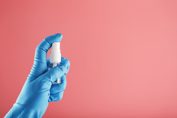 A blue-gloved hand holds a disinfectant on a pink background. Antiseptic treatment of hands from bacteria Sanitizer.