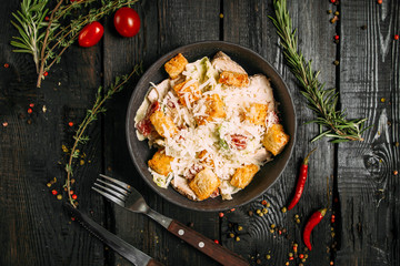Top view on fresh caesar salad of vegetables, chicken and cheese in a dark bowl on the dark wooden background, horizontal