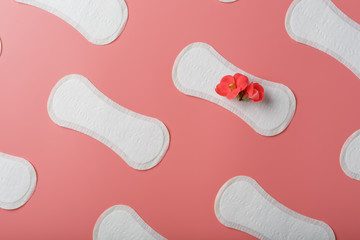 Sanitary pads on a pink background in the form of a diagonal pattern of repetitions, with a red flower on the pad.